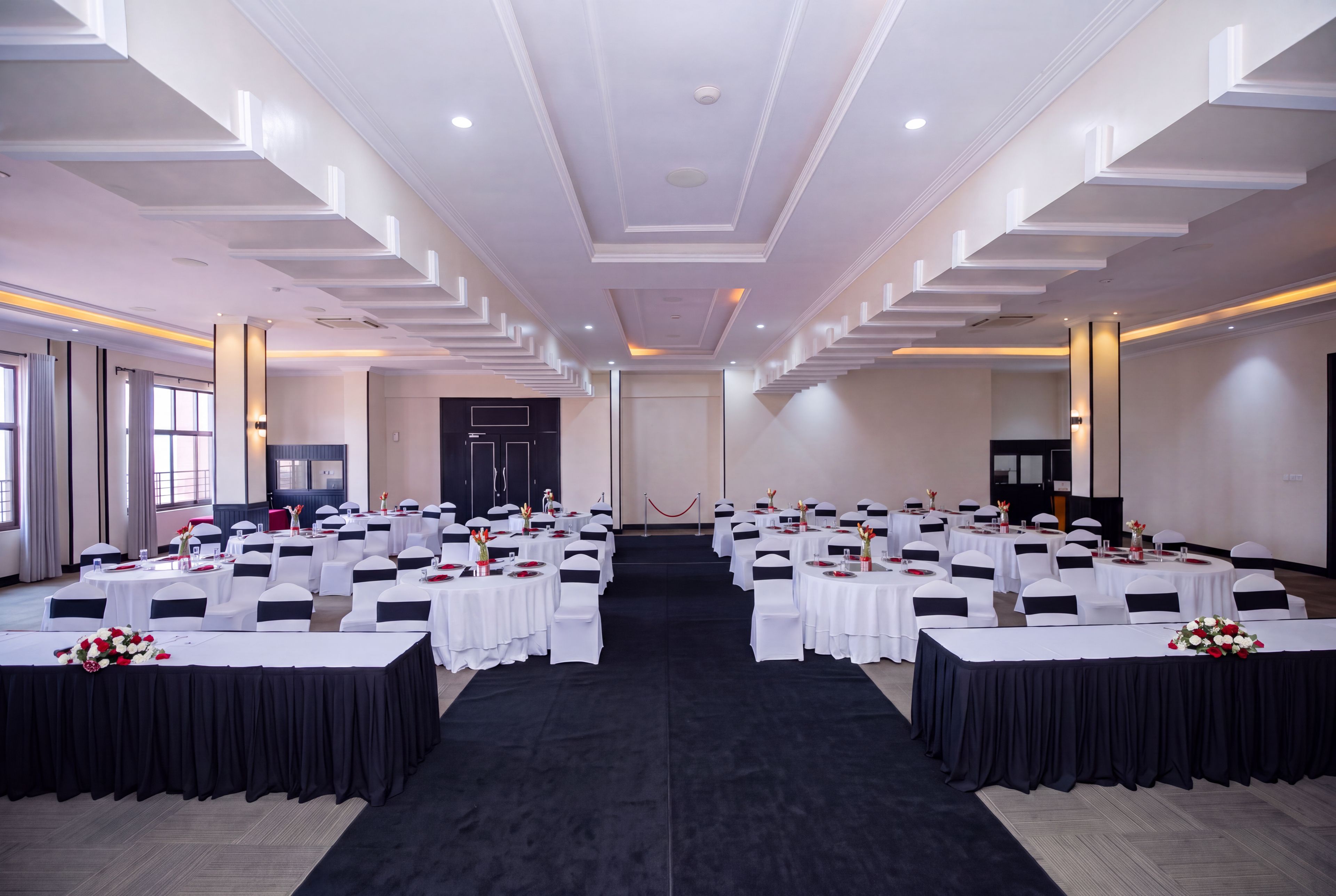Une salle de conférence dotée de plusieurs tables rondes, de nappes blanches et de rubans noirs décorant les chaises.
