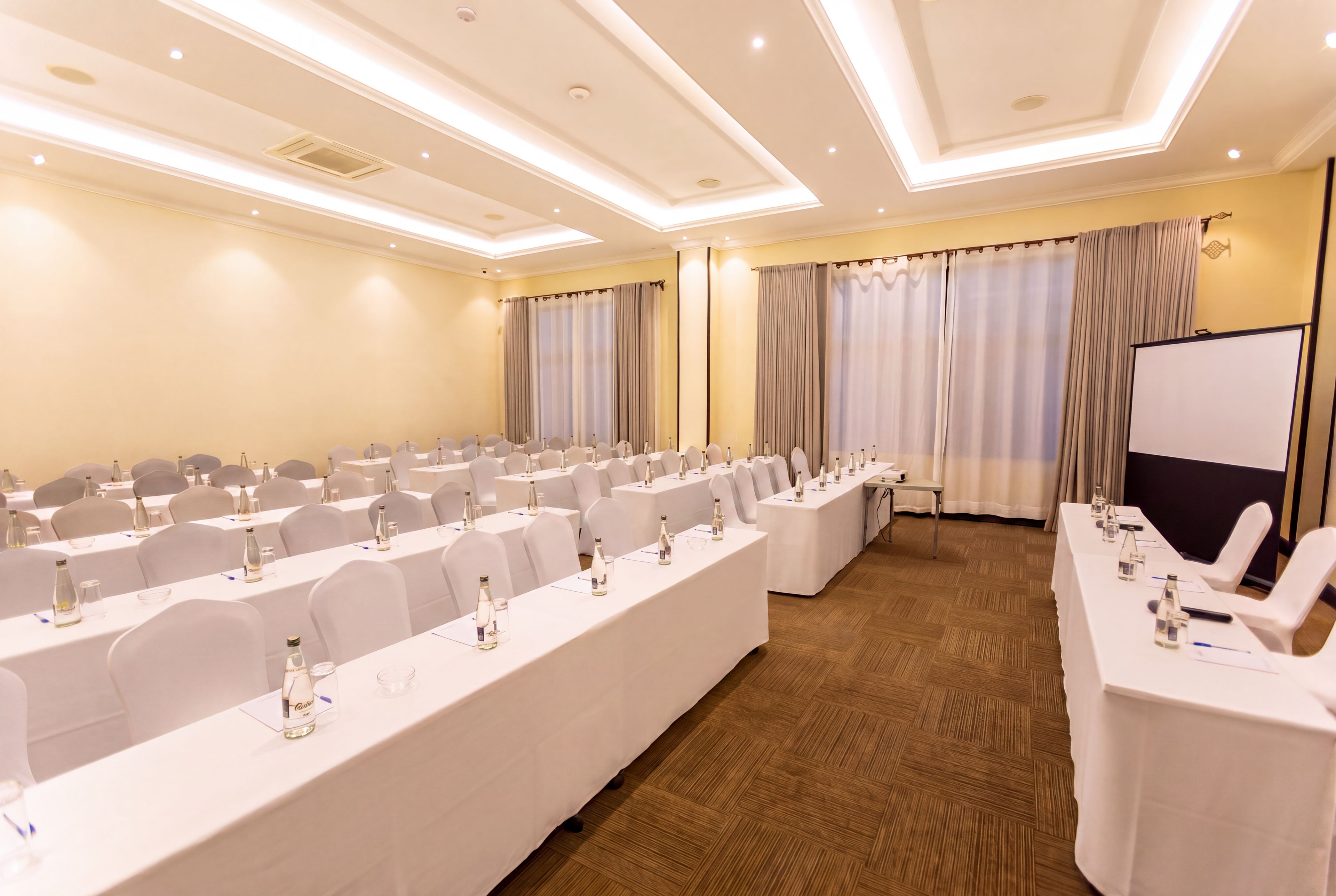 A conference room with long tables, chairs, and a presentation screen.