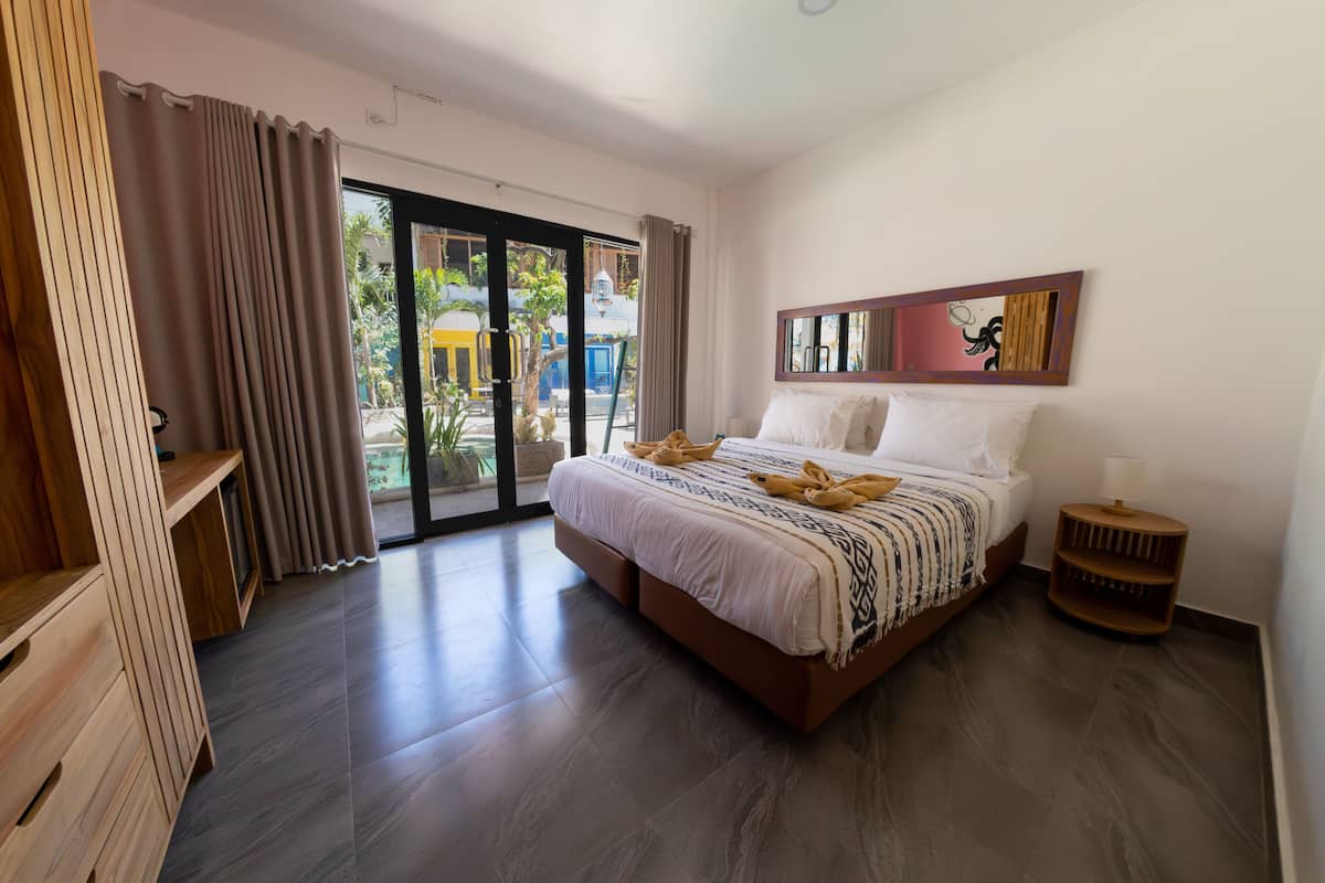 A modern bedroom with a large bed, a wooden nightstand, and a view of the outdoors.