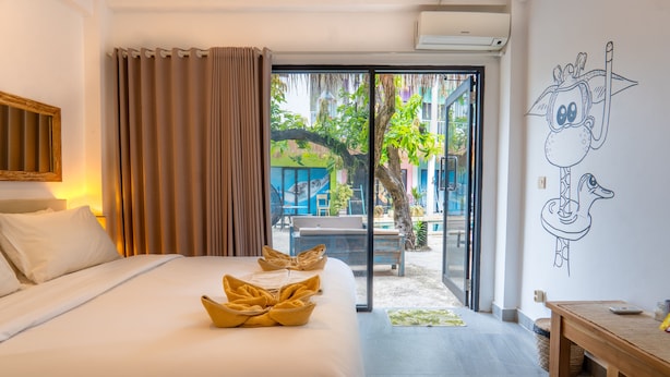 A hotel room with a bed, a wooden bench, a wall mural, and a sliding glass door leading to an outdoor area. - Dragon Dive Komodo Dive Resort (Labuan Bajo)