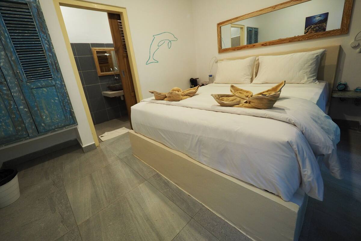 A hotel room with a bed, a bathroom, a mirror, and a dolphin wall art.