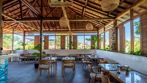 A spacious outdoor dining area with wooden tables and chairs, large windows, and hanging woven light fixtures. - Dragon Dive Komodo Dive Resort (Labuan Bajo)