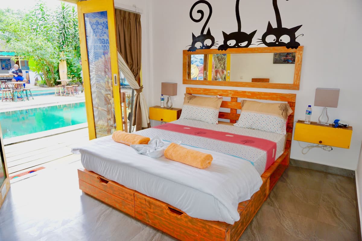 A bedroom with a bed, a nightstand, a mirror, and a view of an outdoor pool.
