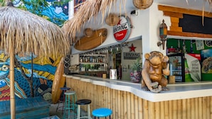 A bar area with a wooden counter, stools, and a decorative monkey statue. - Dragon Dive Komodo Dive Resort (Labuan Bajo)