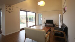 Una sala de estar amplia con un gran ventanal corredizo que da a un patio, un televisor de pantalla plana, un sofá de cuero y una mesa de centro de madera.