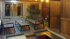 Una terraza al aire libre con mobiliario de madera y luces colgantes.