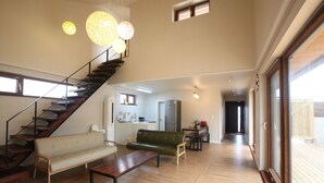 Un amplio salón con una escalera, un sofá, una mesa de centro y una mesa de comedor.