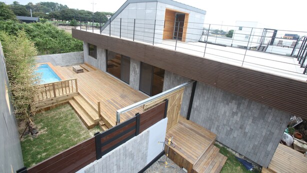 Un edificio residencial moderno con una terraza en la azotea, una piscina y una zona de deck de madera.