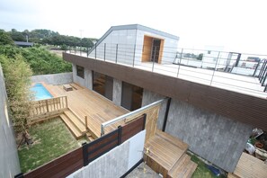 Un edificio residencial moderno con una terraza en la azotea, una piscina y una zona de deck de madera.