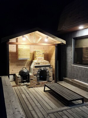 Una estructura de madera al aire libre con un horno de ladrillo, una parrilla y un banco.