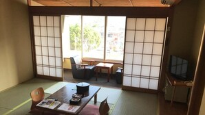A tatami mat room with a low table, chairs, and a television. - Itoen Hotel Bekkan (Ito)