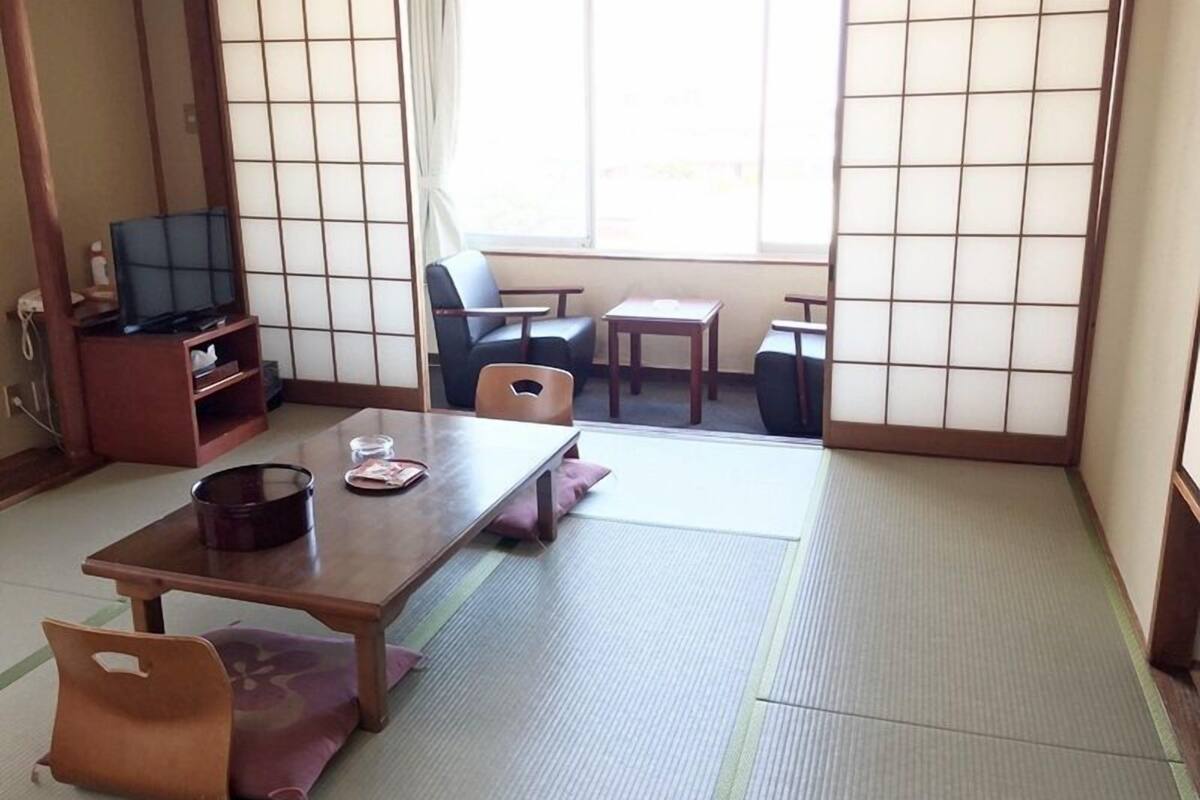 A traditional Japanese room with tatami flooring, a low table with cushions, a television, and sliding doors.