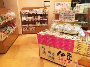 A store interior with shelves stocked with packaged goods, a display counter with boxes, and a framed certificate on the wall.