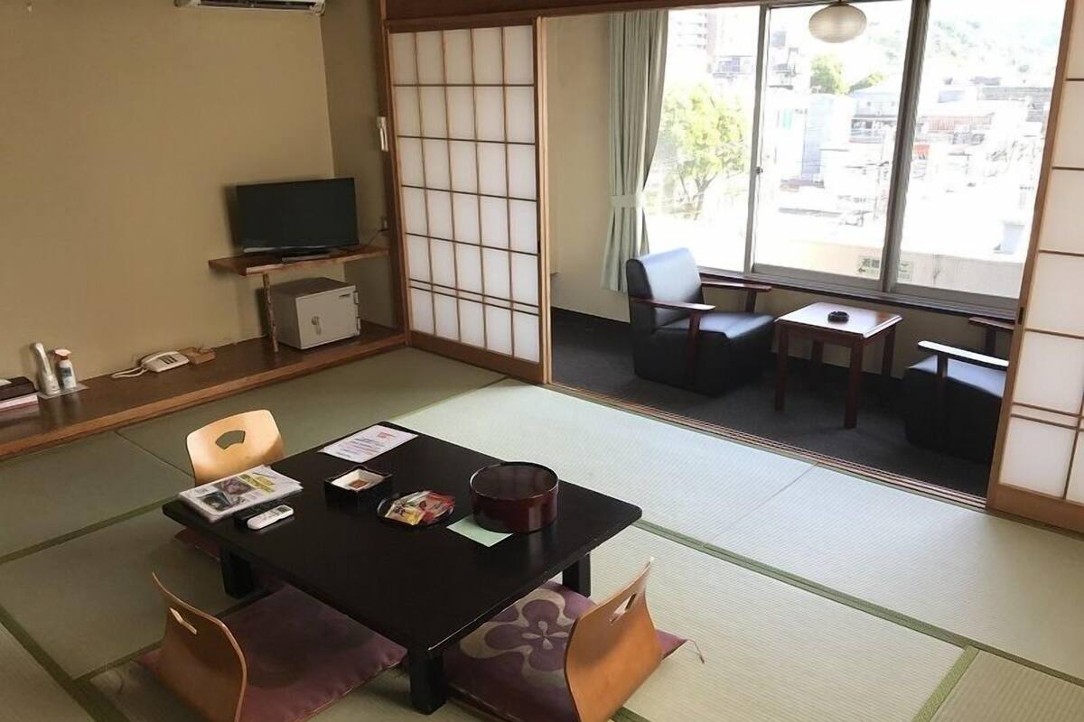 A traditional Japanese-style room with tatami flooring, a low table with cushions, a television, and a sliding door leading to a balcony.