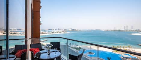 A balcony with wicker furniture, a glass table, and a view of a beach and water body.