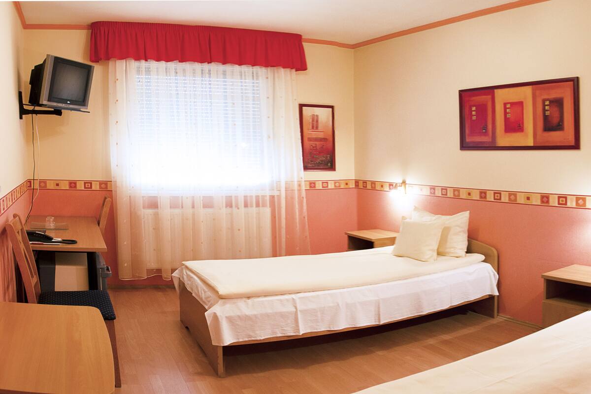 Ein Hotelzimmer mit Bett, Schreibtisch, Stuhl, Fernseher und einem fensterbepflanzten Fenster.