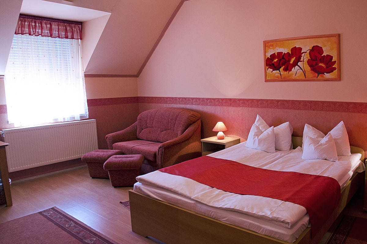 Ein Schlafzimmer mit Bett, Stuhl, Nachttisch, Lampe und einem Gemälde an der Wand.