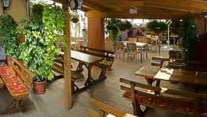 Ein Essbereich im Freien mit Holztischen und -bänken, umgeben von Topfpflanzen und hängenden Grünpflanzen.