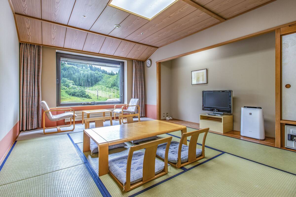 A traditional Japanese-style room with tatami flooring, a wooden dining table, and a television.