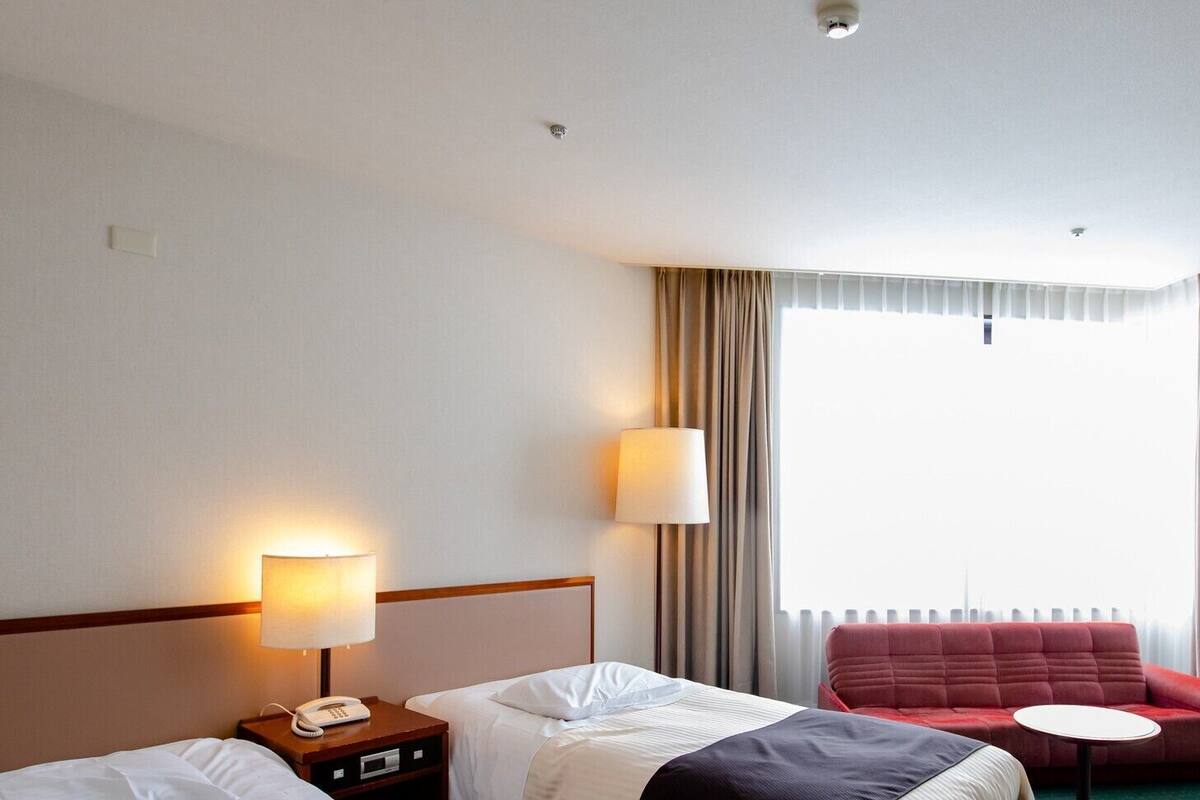 A hotel room with two beds, a red sofa, a small round table, and a window with curtains.