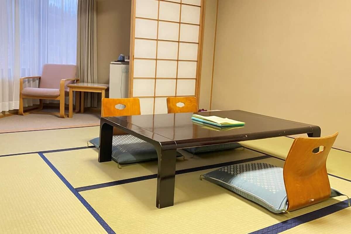 Une pièce avec un sol recouvert de tatamis, une petite table basse, quatre chaises, un petit meuble et une porte coulissante.