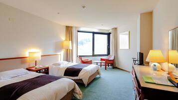 A hotel room with two beds, a desk, a chair, a desk lamp, a telephone, and a window with curtains.