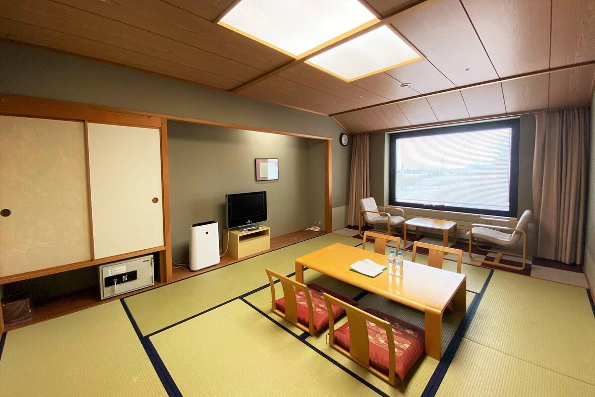 A traditional Japanese-style room with tatami flooring, a television, a desk, and a large window with curtains.