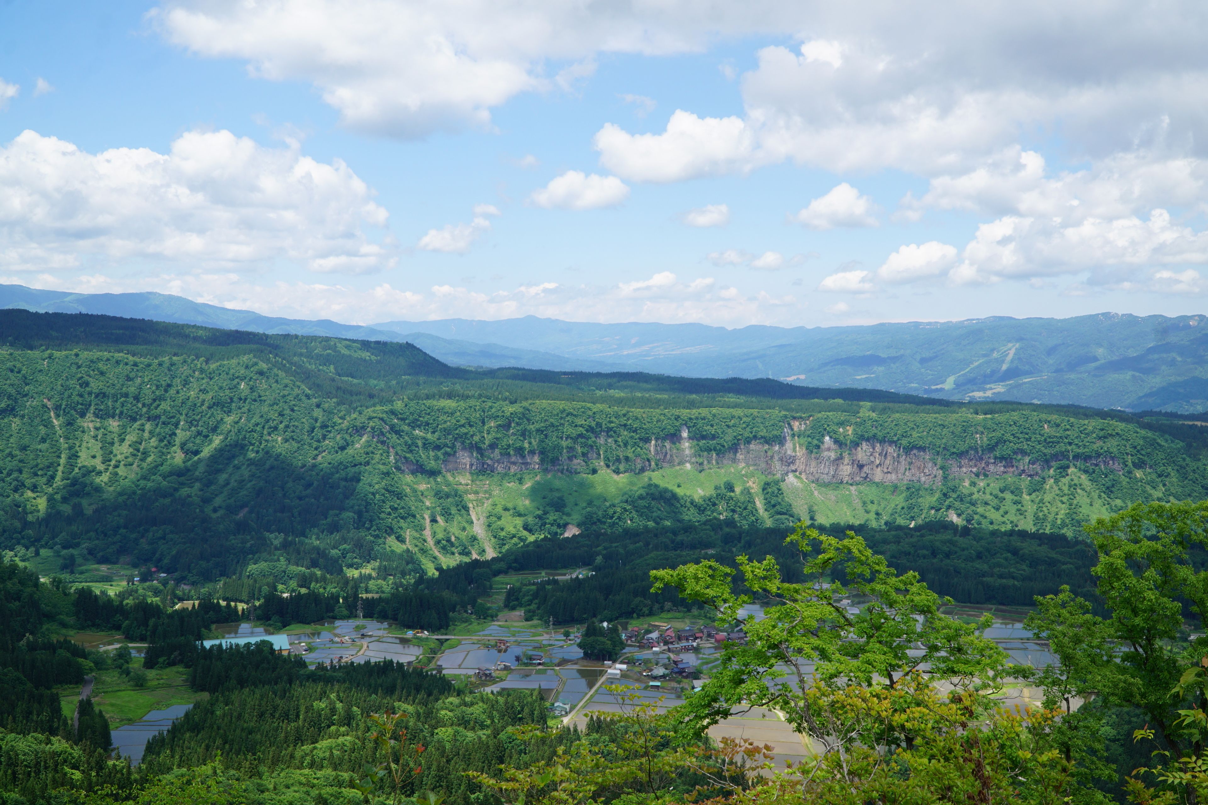 Une vue panoramique d’un paysage montagneux, avec une rivière et de petits bâtiments dans la vallée.