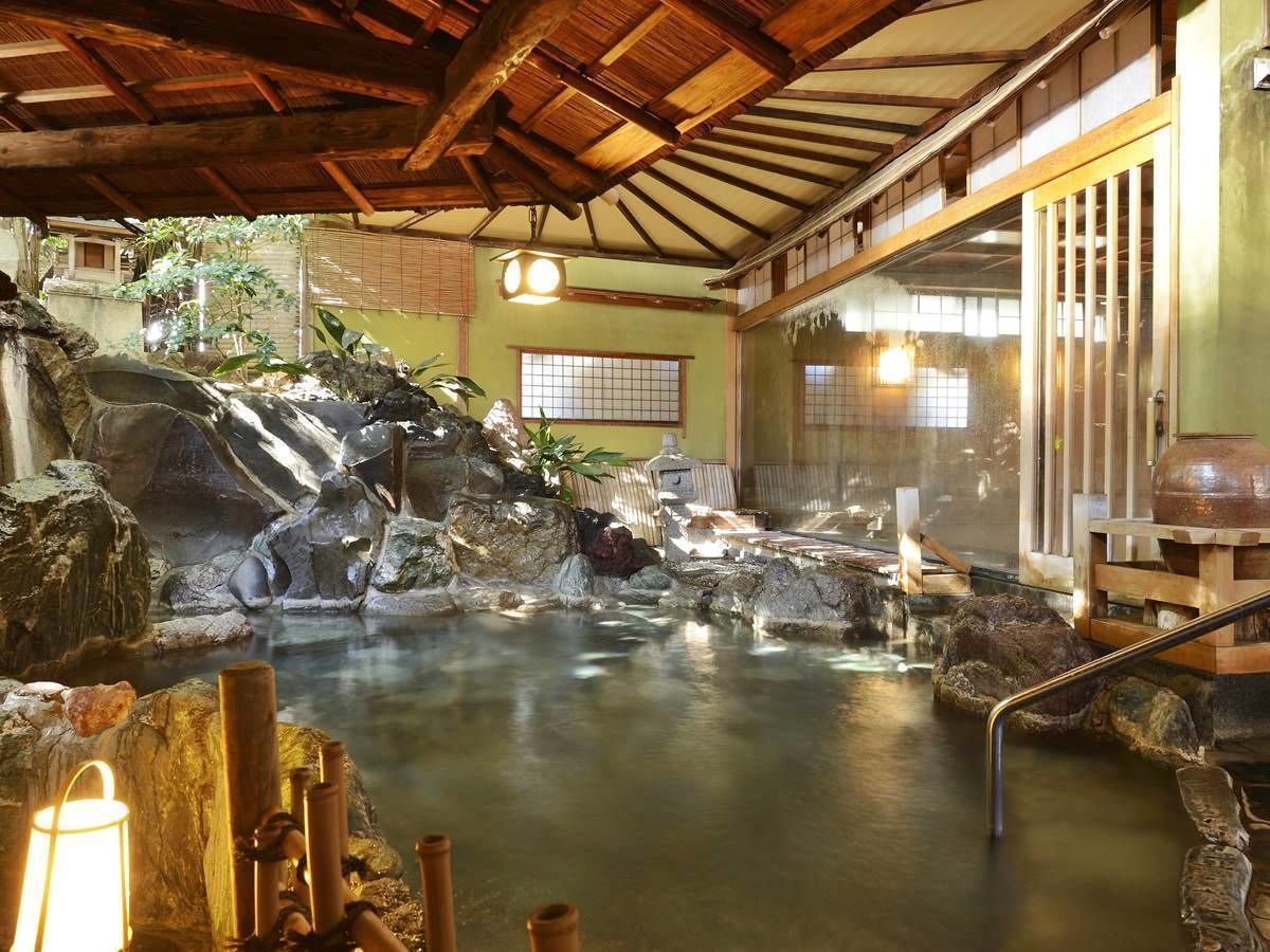 A traditional Japanese onsen with a rock garden, wooden benches, and a wooden ceiling.
