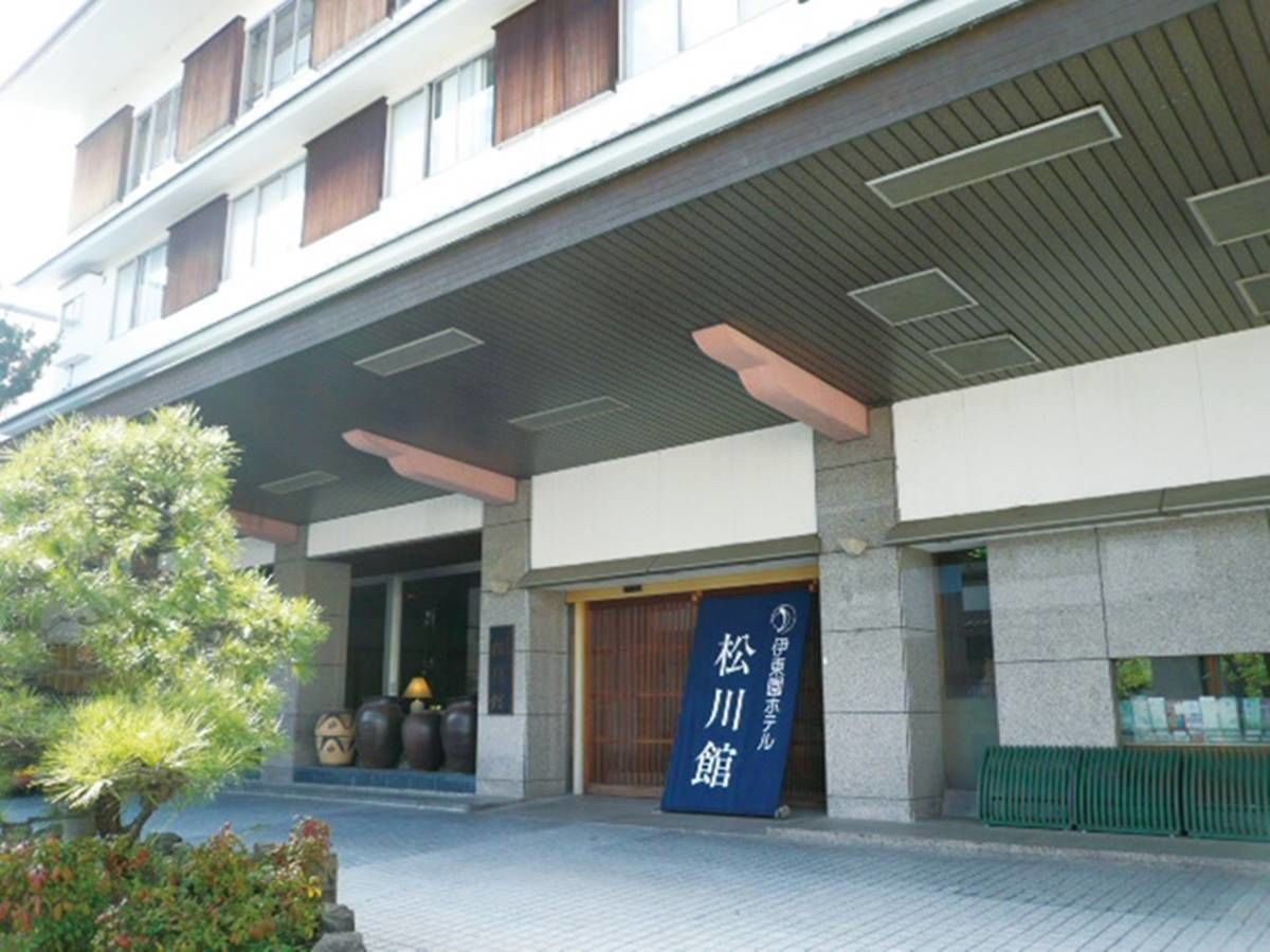 A modern building with a large entrance, a signboard, and a well-maintained garden area.
