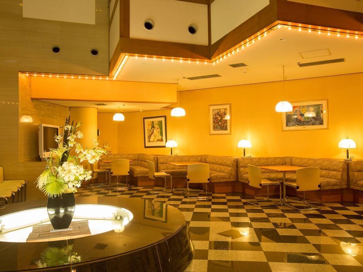 A hotel lobby with a checkered floor, seating areas, and a central table with a vase of flowers.