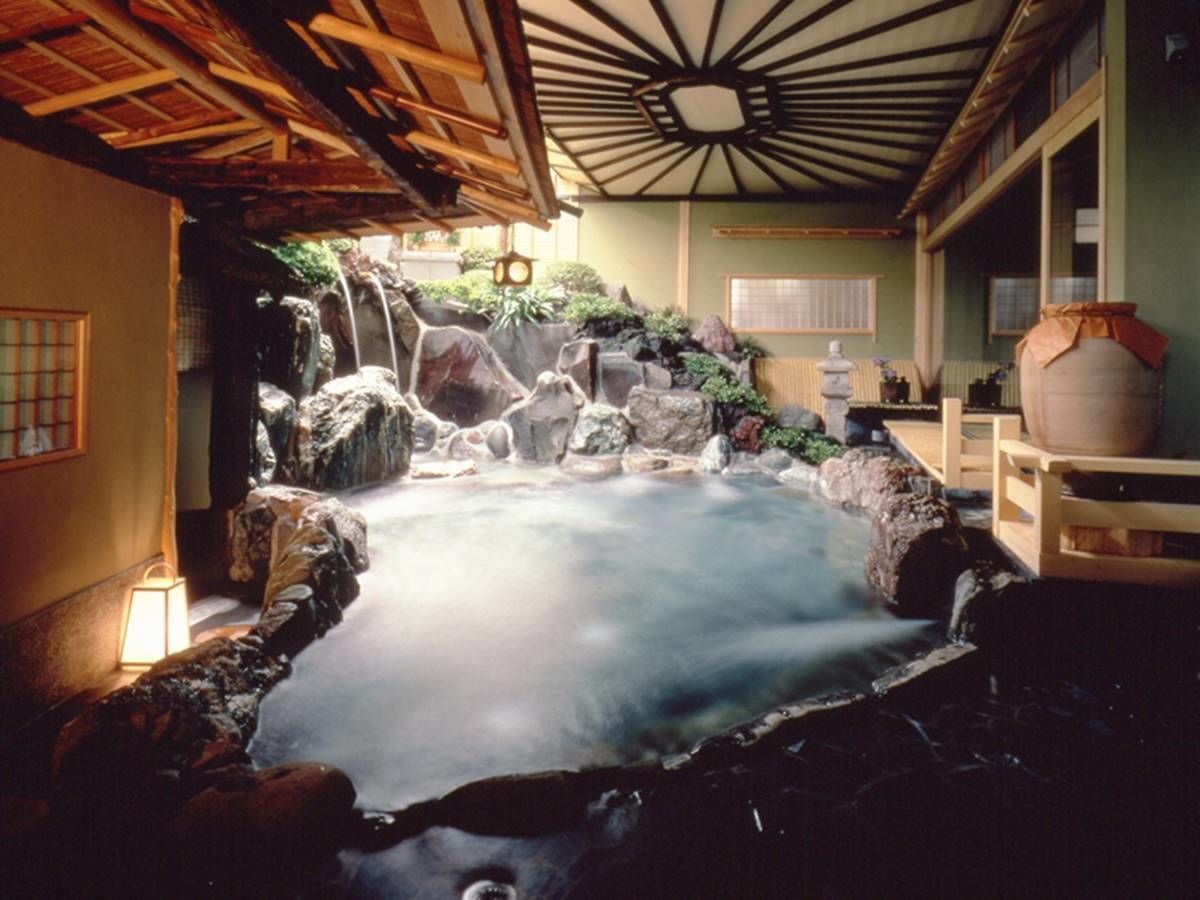 A hot spring bath with a wooden ceiling and a view of a rocky landscape.