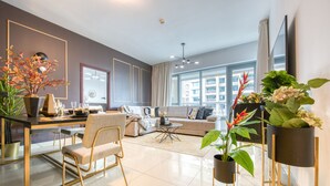 A modern living room with a sofa, coffee table, and chairs. There are plants and a TV mounted on the wall. - Maison Privee - Radiant Urban Retreat with Iconic Burj Khalifa Vws (Dubai)