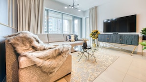 A modern living room with a sofa, a glass coffee table, a flat-screen TV, and a decorative vase. - Maison Privee - Radiant Urban Retreat with Iconic Burj Khalifa Vws (Dubai)