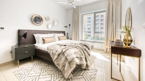 A modern bedroom with a large bed, a nightstand, a desk, and a window with a view of buildings. - Maison Privee - Radiant Urban Retreat with Iconic Burj Khalifa Vws (Dubai)