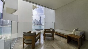 Una sala de estar moderna con una pared de vidrio, muebles de madera y vistas a un horizonte urbano.