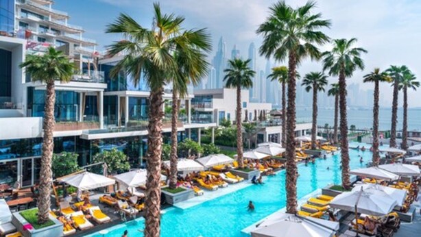 Un área de piscina en la azotea con palmeras, sillas de descanso y vistas del horizonte de la ciudad.