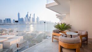 Un balcón moderno con barandilla de cristal que ofrece vistas a un horizonte urbano y una masa de agua.