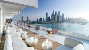 Un salón en la azotea con asientos blancos y vistas a un horizonte urbano.