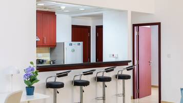 A modern kitchen with a central island, bar stools, a potted plant, and a red door.