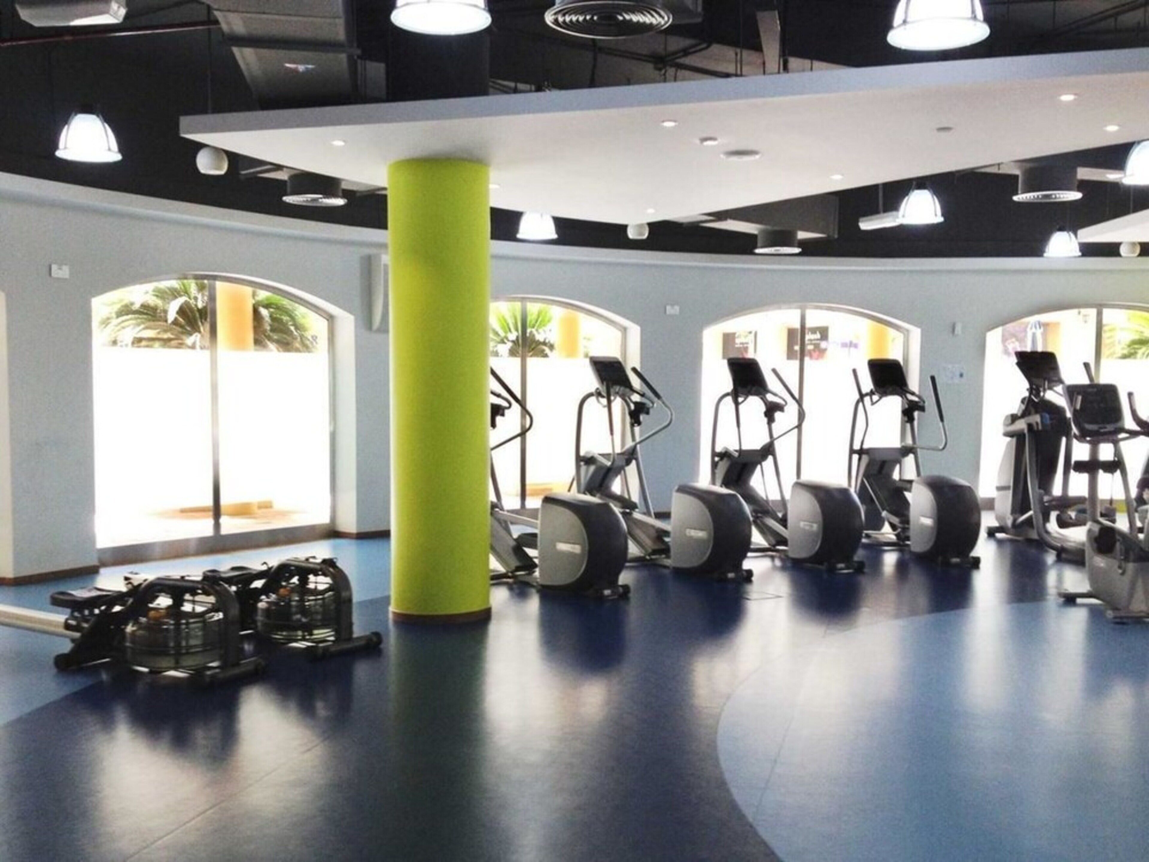 A gym with exercise equipment, large windows, and a green pillar.