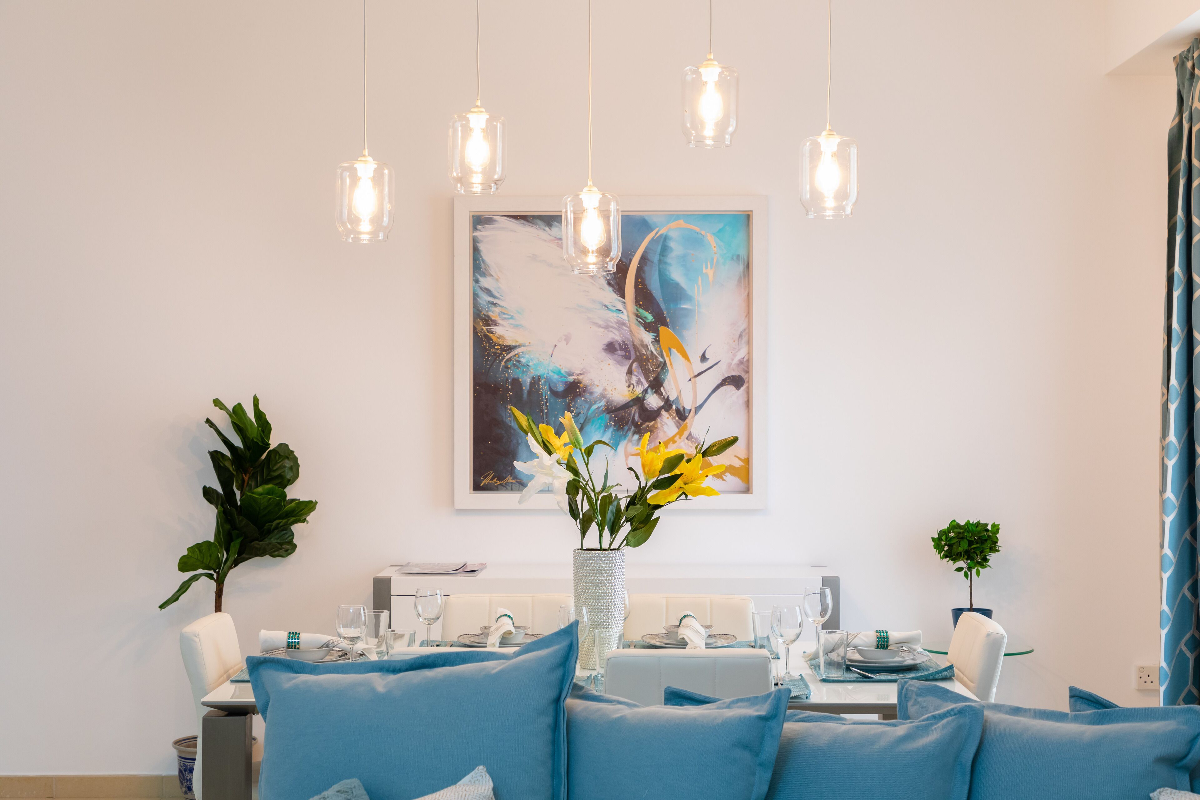 A dining area with a table set for four, a vase with flowers, and a painting on the wall.