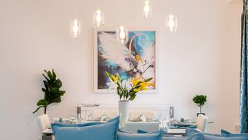 A dining area with a table set for four, a vase with flowers, and a painting on the wall.