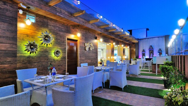 An outdoor dining area with wicker furniture and a wooden wall. - The Gold Regency (New Delhi)