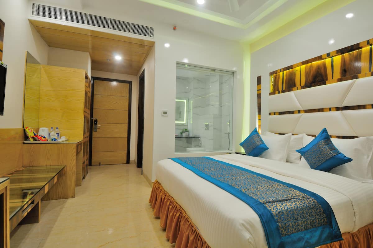 A hotel room with a large bed, a wooden desk, a glass shower area, and a wooden door.