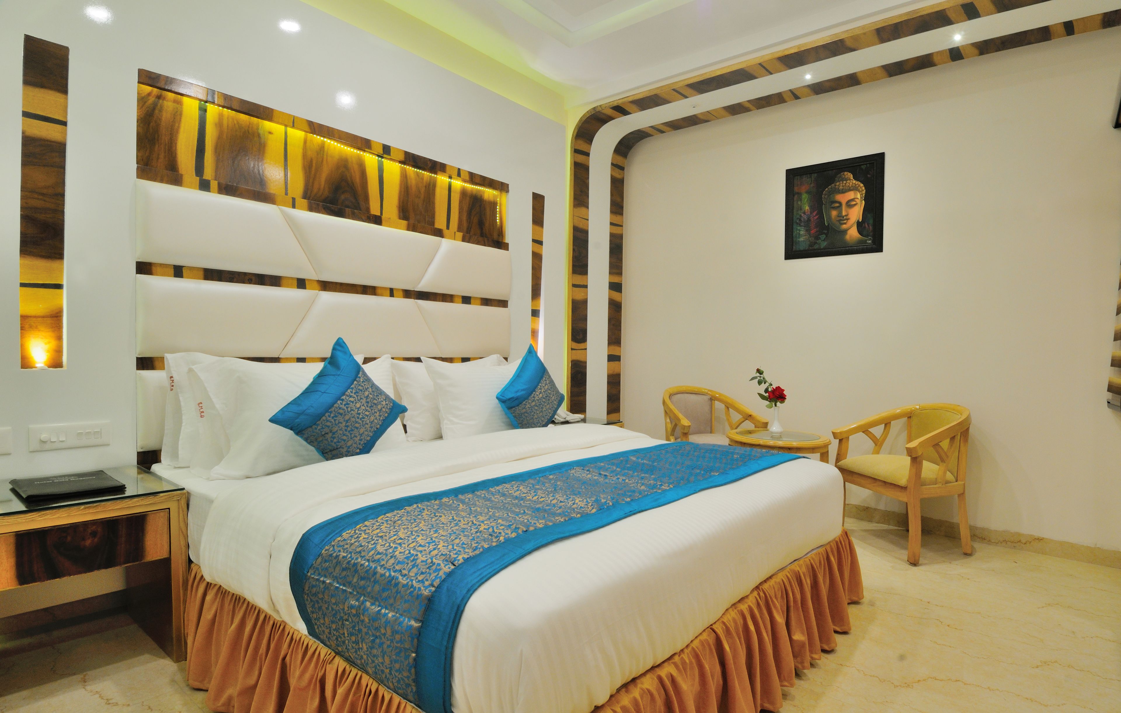 Habitación de hotel con una cama grande, cabecera con acabado en madera clara, una mesita con un florero y una silla.