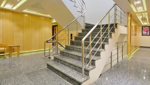 A modern hotel lobby with a granite staircase, metal railings, and a wooden wall. - The Gold Regency (New Delhi)
