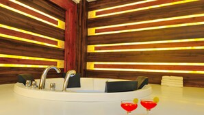 A modern bathroom with a central sink, multiple faucets, and a large mirror. There are two red drinks on the counter. - The Gold Regency (New Delhi)