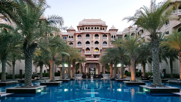 A large, rectangular swimming pool with a geometric tile pattern, surrounded by palm trees and a multi-story building with traditional architecture. - Maison Privee - Charming Apt with Arabesque Sea View on the Palm Jumeirah (Dubai)