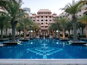A large, rectangular swimming pool with a geometric tile pattern, surrounded by palm trees and a multi-story building with traditional architecture. - Maison Privee - Charming Apt with Arabesque Sea View on the Palm Jumeirah (Dubai)